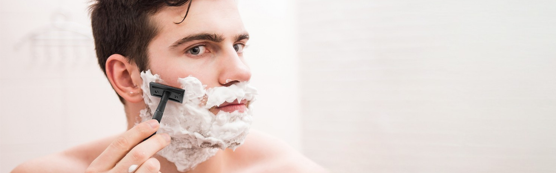 Man shaving with a bambaw razor and shaving cream on a plain background